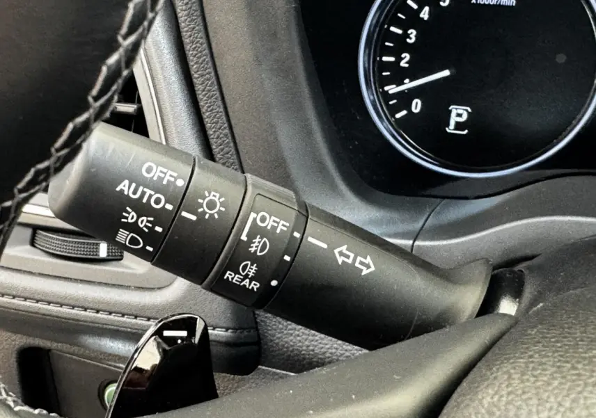 Gros plan sur la commande des phares et clignotants du tableau de bord noir du Honda HR-V blanc.