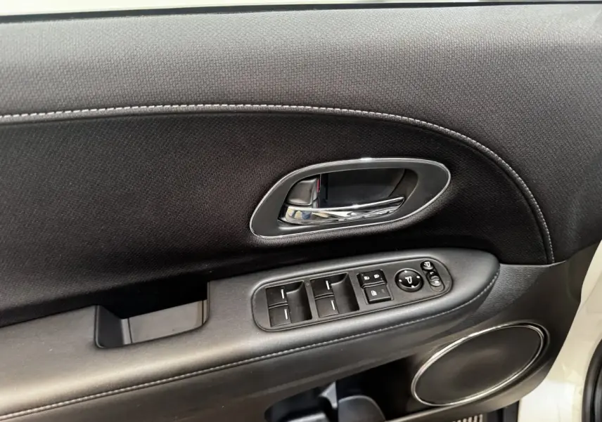 Gros plan sur la porte avant gauche noire avec commandes électriques et poignée chrome d’un Honda HR-V blanc.