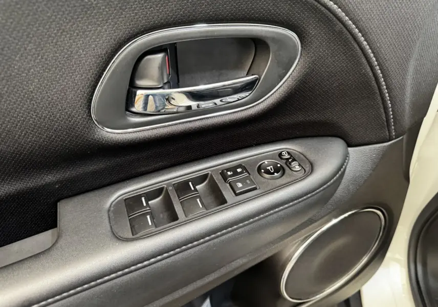 Gros plan sur la porte côté conducteur du Honda HR-V blanc, montrant les commandes des vitres et le haut-parleur rond chromé.