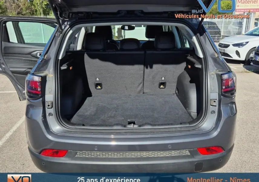 Coffre ouvert en vue arrière d’un Jeep Compass gris 2024 avec hayon relevé et porte arrière gauche ouverte.