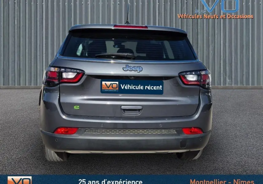 Vue arrière d'un Jeep Compass gris 2024 avec feux LED et logo e-Hybrid visible sur un parking extérieur.