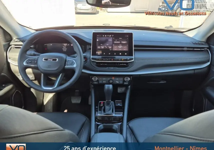 Intérieur du Jeep Compass 2024 gris, vue frontale du tableau de bord avec écran tactile et volant multifonction.