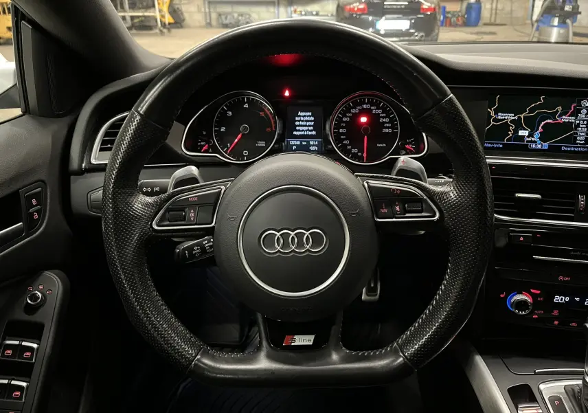 Vue centrée sur le volant S line noir de l'Audi A5 Sportback 2015 avec tableau de bord et écran de navigation allumés.