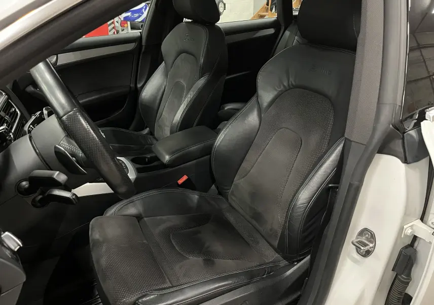 Vue intérieure côté conducteur d'une Audi A5 Sportback blanche, sièges sport en cuir noir S line avec volant partiellement visible.