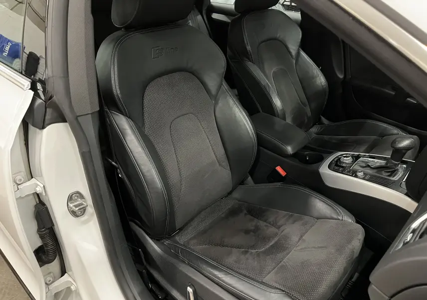 Vue intérieure côté conducteur de l'Audi A5 Sportback blanche, sièges sport S line en cuir noir avec console centrale visible.