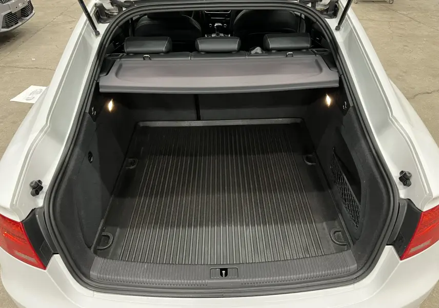 Coffre ouvert vu de l'arrière d'une Audi A5 Sportback blanche de 2015, avec tapis de sol noir et banquette arrière visible.