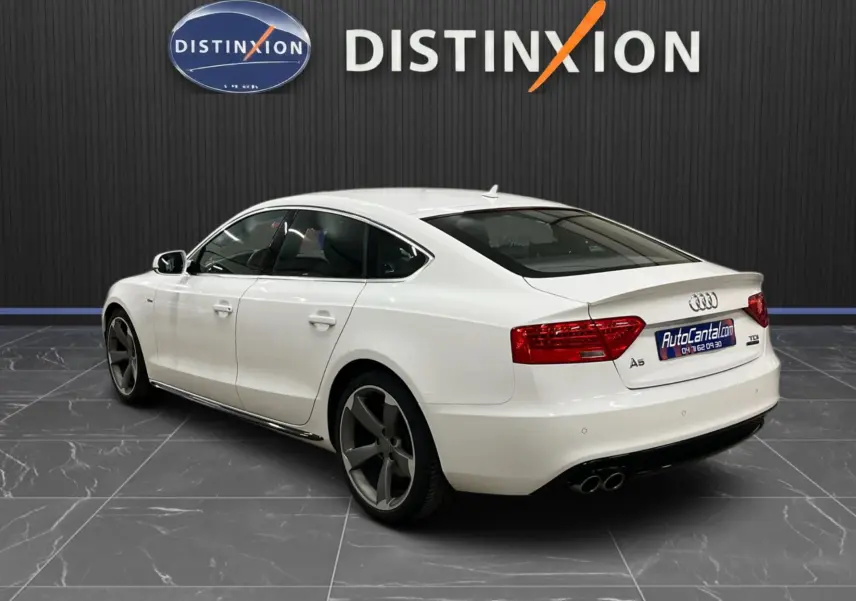 Audi A5 Sportback blanc vue 3/4 arrière droit, jantes 5 branches foncées et double sortie d'échappement chromée.