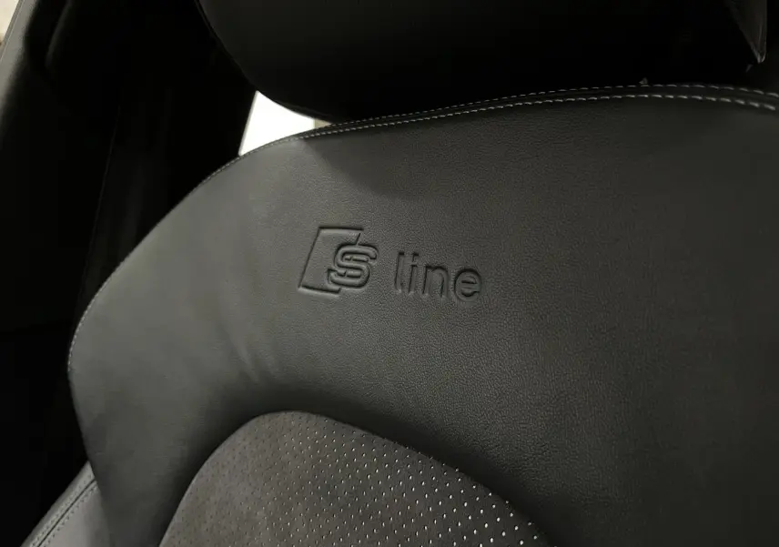 Gros plan sur le siège avant noir en cuir et alcantara avec logo S line embossé dans une Audi A5 Sportback blanche.