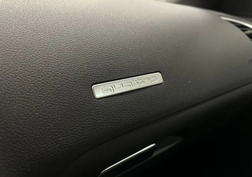 Gros plan sur le badge Quattro argenté sur le tableau de bord noir de l'Audi A5 Sportback blanc.