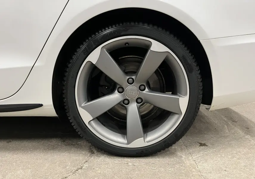 Gros plan sur la roue arrière droite d’une Audi A5 Sportback blanche, jante alliage 5 branches grises.
