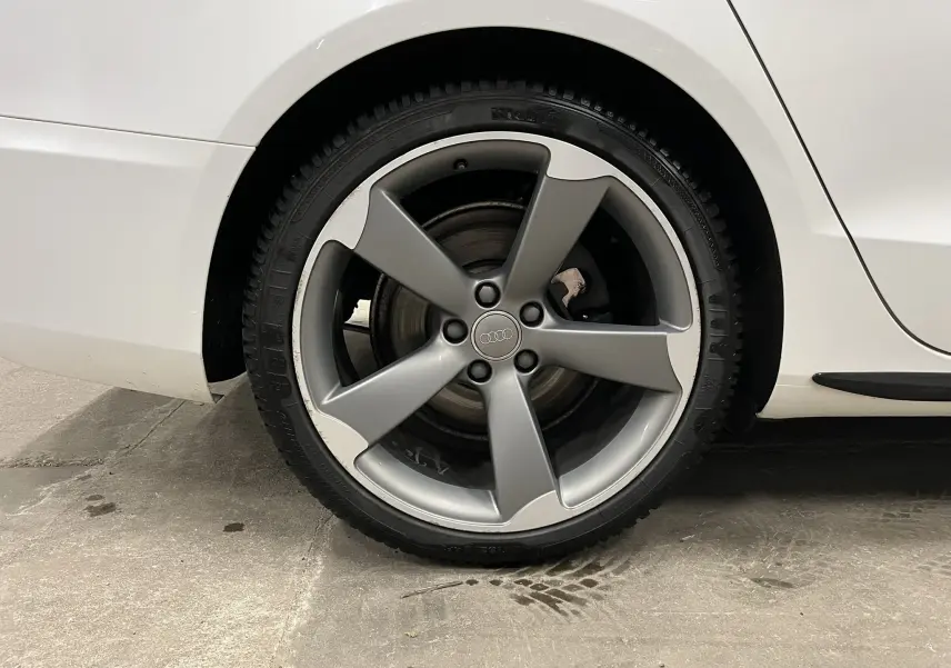 Gros plan sur la roue arrière droite de l'Audi A5 Sportback blanche avec jante alliage grise à cinq branches.