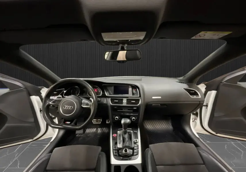 Vue intérieure avant de l'Audi A5 Sportback blanche 2015, tableau de bord et volant avec portes ouvertes.