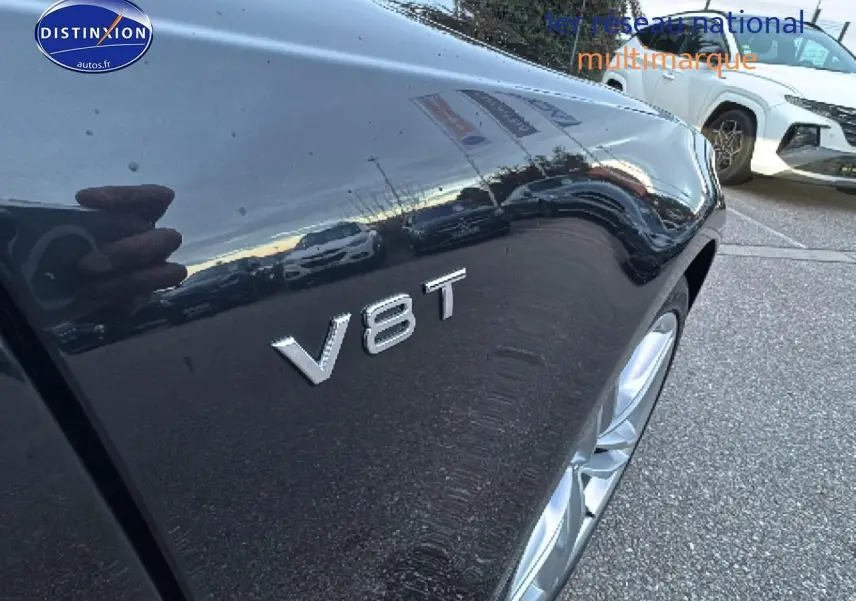 Gros plan sur l'aile avant droite noire d'une Audi S7 Sportback avec l'insigne V8T visible au-dessus de la roue.
