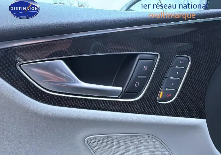 Gros plan sur la poignée intérieure côté gauche en aluminium et garniture carbone du panneau de porte gris clair d’une Audi S7 Sportback noire.