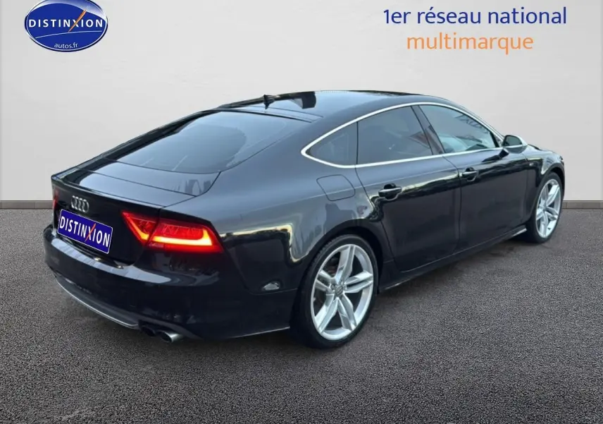 Audi S7 Sportback noir vue 3/4 arrière droit avec jantes alu et feux arrière allumés sur sol gris.
