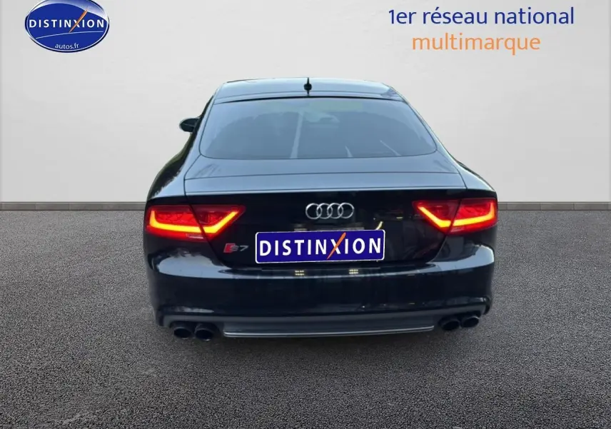 Vue arrière d'une Audi S7 Sportback noire avec feux allumés et double sortie d'échappement chromée.