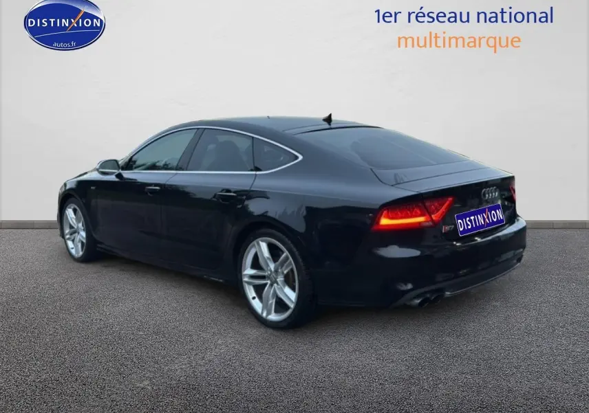 Audi S7 Sportback noir vue 3/4 arrière droit avec jantes alu et feux arrière allumés.