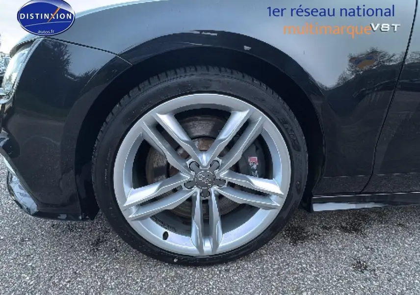 Gros plan sur la roue avant gauche argentée avec logo Audi, sur une carrosserie noire brillante d'Audi S7 Sportback.
