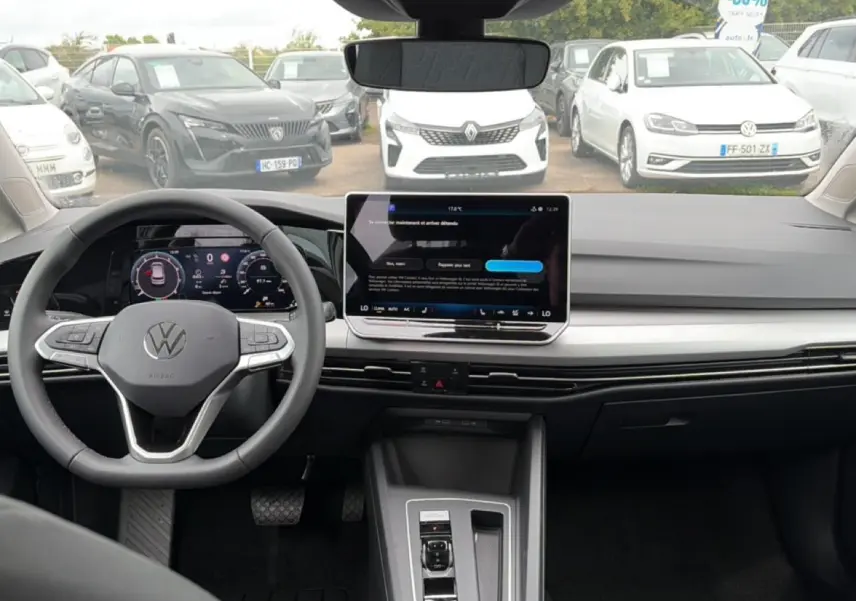 Vue intérieure avant de la Volkswagen Golf 2026, tableau de bord moderne avec écran tactile central et volant multifonction gris.