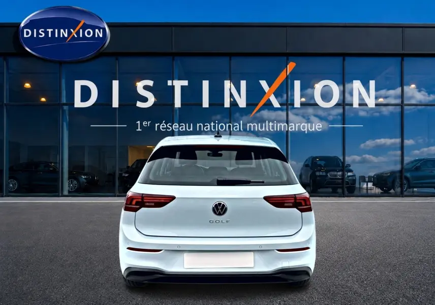 Vue arrière d'une Volkswagen Golf 2026 bleu glacier garée devant une vitrine avec logo Distinxion.