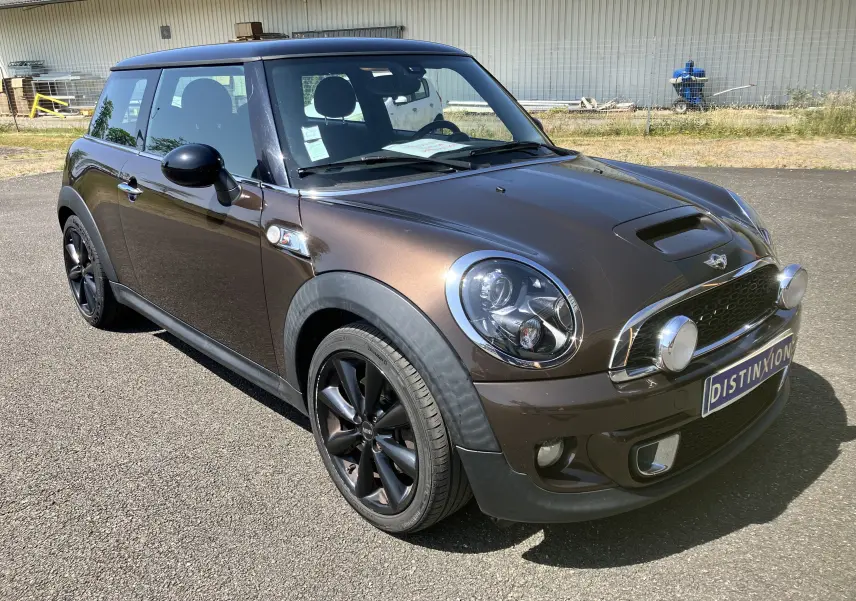 MINI Cooper S R56 marron vue 3/4 avant droit avec phares additionnels et jantes noires sur parking.
