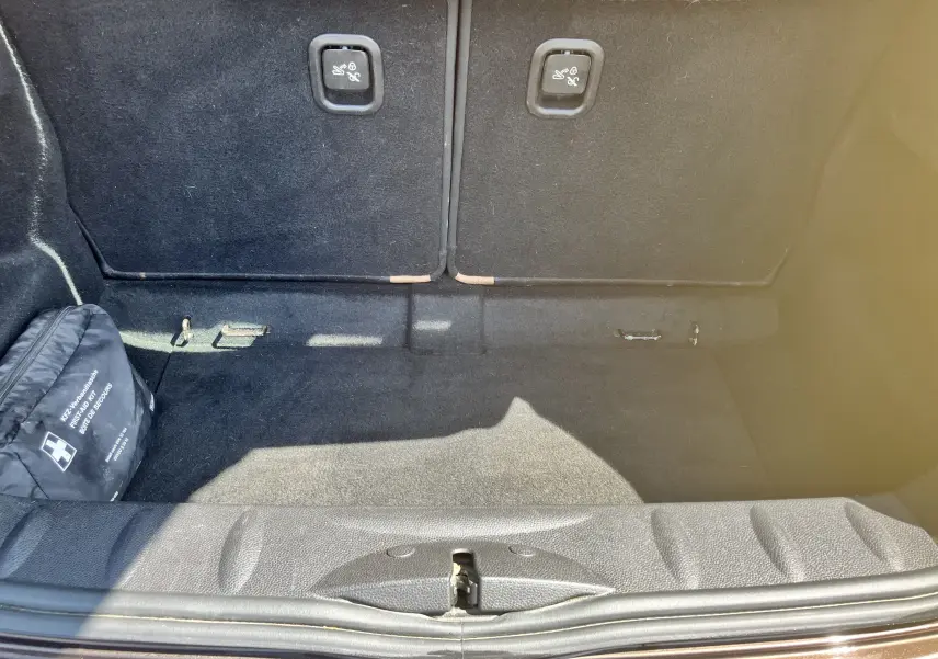 Coffre ouvert d'une MINI Cooper S R56 marron 2012, vue intérieure montrant le tapis noir et un kit de secours à gauche.