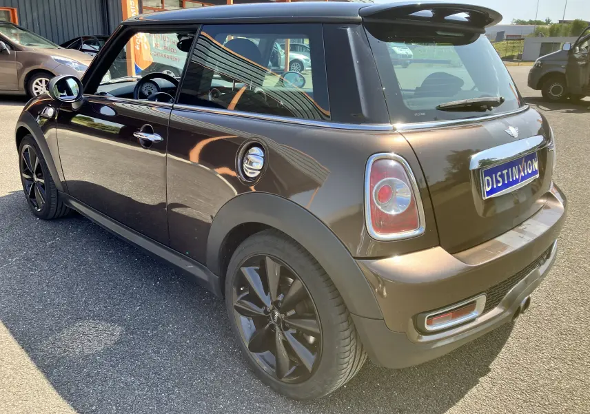Vue 3/4 arrière droite d'une MINI Cooper S R56 marron 2012 avec jantes noires et toit noir brillant.
