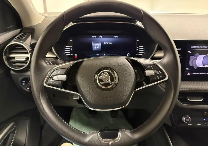 Vue intérieure centrée sur le volant cuir noir de la Skoda Fabia 2023 avec tableau de bord digital et écran d’aide au stationnement.
