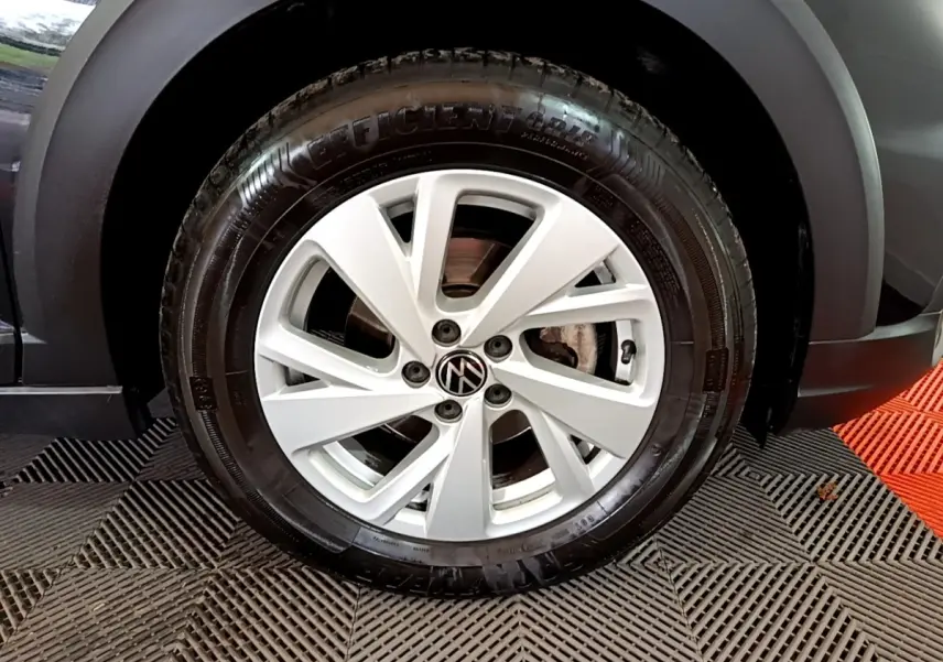 Gros plan sur la roue avant droite d’un Volkswagen Taigo noir, avec jante alliage argentée et logo VW central.