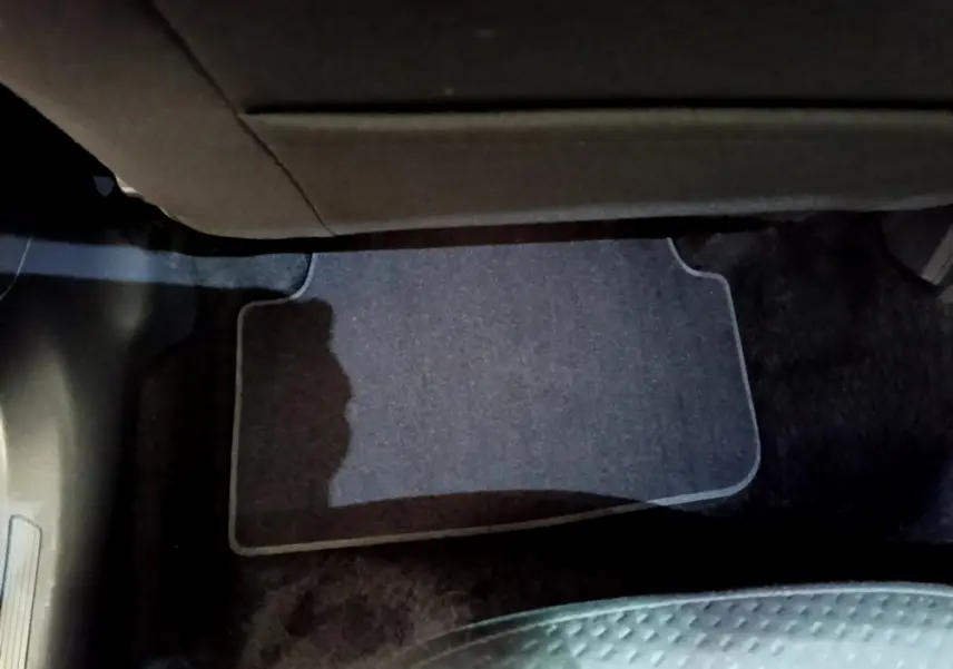 Vue intérieure du plancher côté passager avant avec tapis gris et partie inférieure de la planche de bord visible