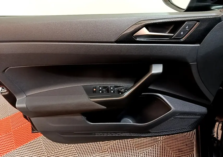 Vue intérieure du panneau de porte avant gauche noir du Volkswagen Taigo 2023 avec commandes électriques et poignée intégrée.