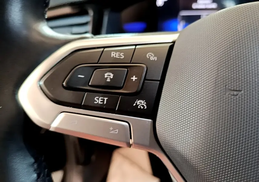 Gros plan sur les commandes du volant alu et cuir du Volkswagen Taigo noir, avec boutons de régulateur de vitesse.