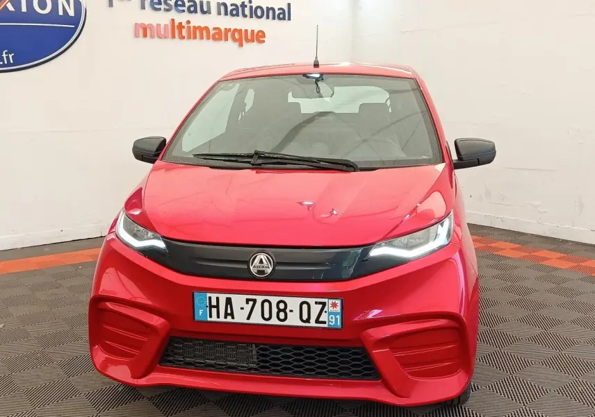 Vue de face d'une Aixam Ambition 0.5 City Pack rouge 2024 avec rétroviseur côté conducteur visible.