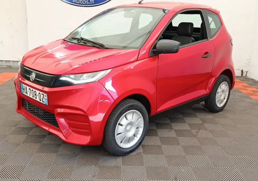 Vue 3/4 avant d'une Aixam Ambition 0.5 City Pack rouge 2024 avec rétroviseur côté conducteur noir.