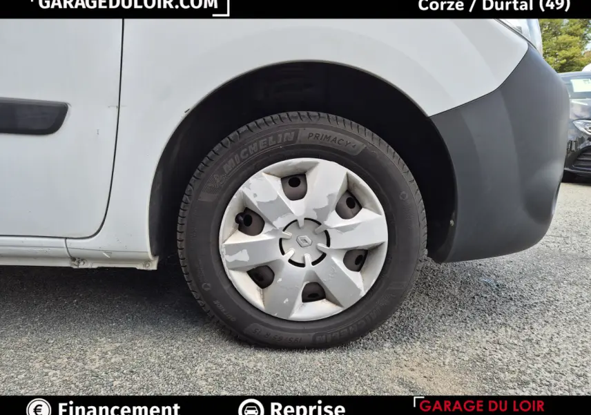 Gros plan sur la roue avant droite d’un Renault Kangoo blanc avec enjoliveur usé et pare-chocs noir.