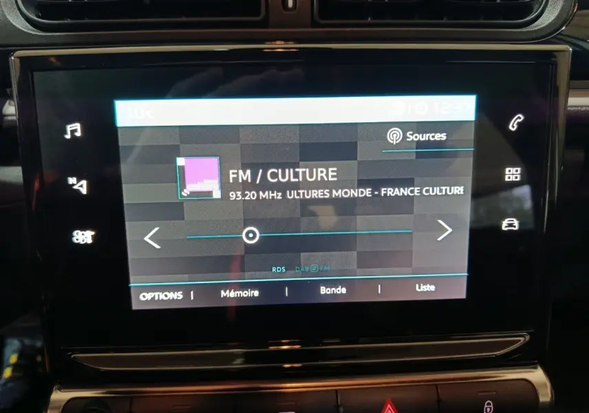 Écran tactile central de la Citroën C3 gris clair 2024 affichant une station FM sur fond noir brillant.