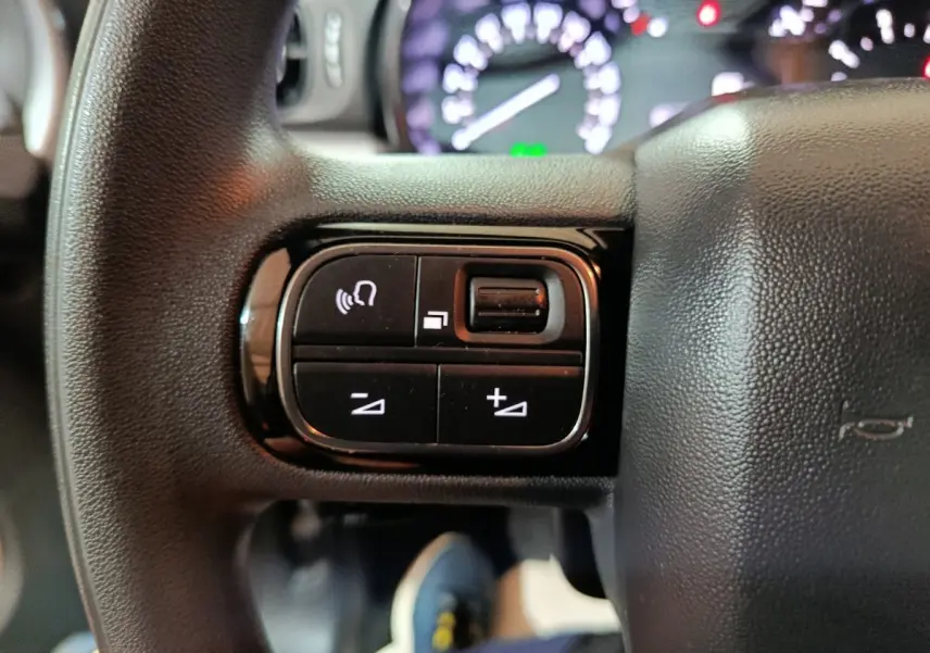 Gros plan sur les commandes gauche du volant noir de la Citroën C3 2024, avec tableau de bord flou en arrière-plan.