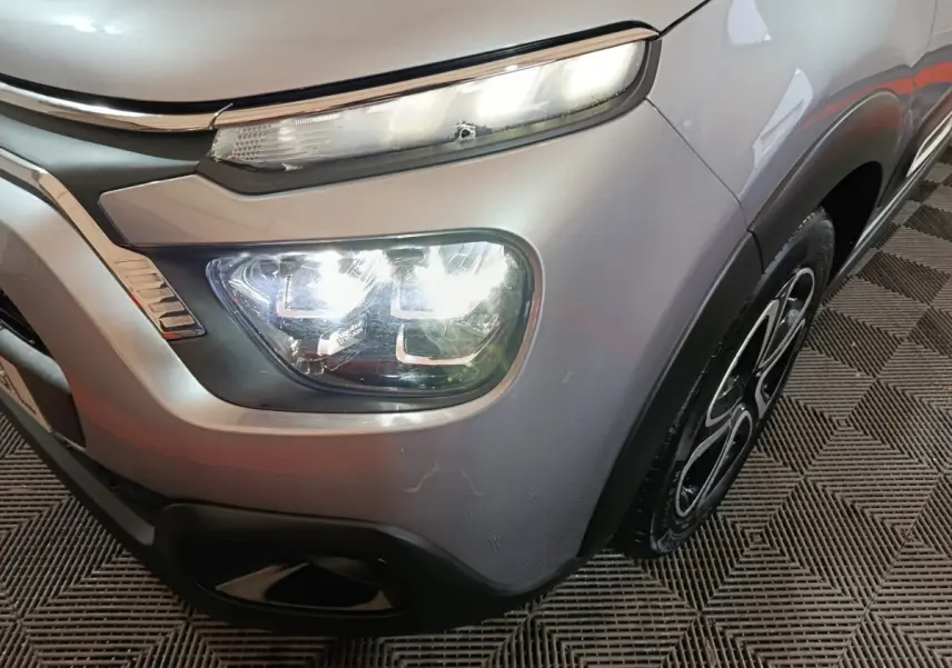 Gros plan sur l'avant droit gris clair d'une Citroën C3 2024 avec phares LED allumés et jante noire stylisée.
