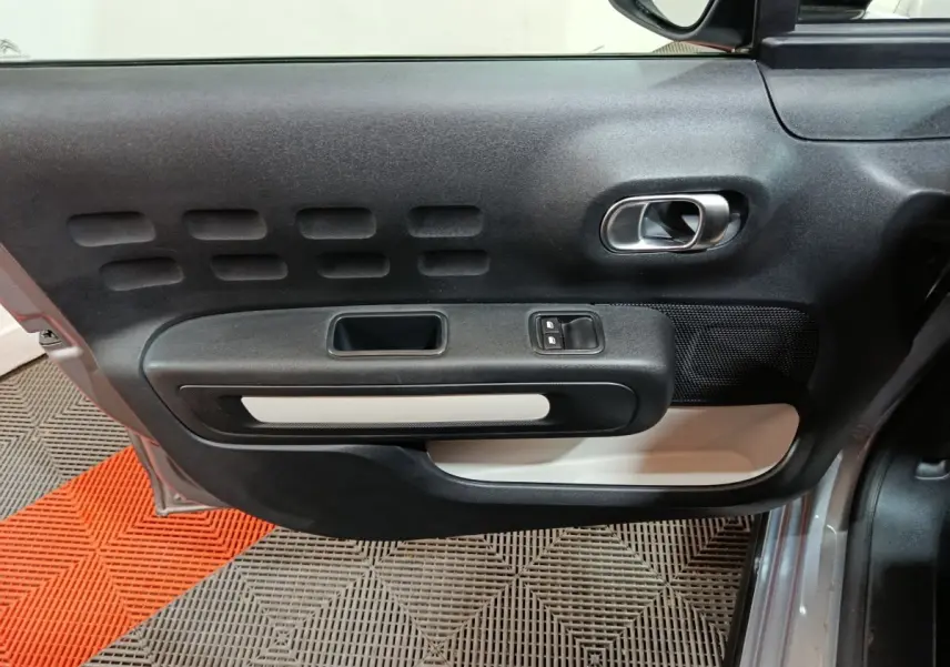 Vue latérale du panneau de porte avant gauche gris clair de la Citroën C3 2024 avec commande de vitres et poignée intégrée.