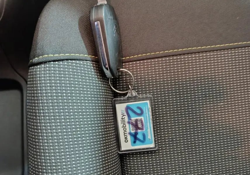 Gros plan sur une clé Citroën posée sur un siège tissu gris clair avec surpiqûres jaunes.