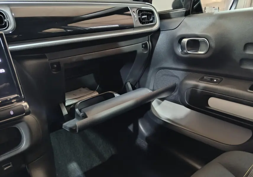 Intérieur avant droit de la Citroën C3 2024 gris clair, avec boîte à gants ouverte et tableau de bord noir brillant.