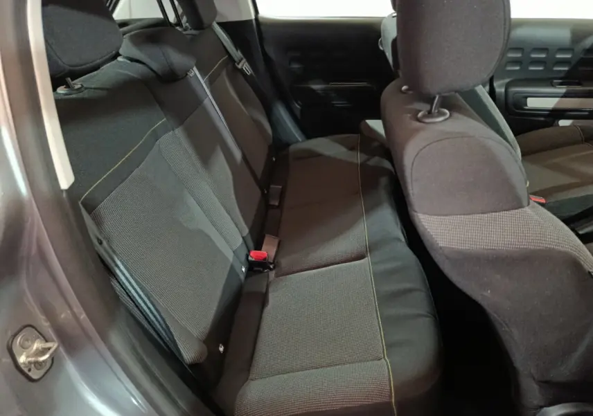 Vue intérieure côté arrière gauche de la banquette noire de la Citroën C3 2024 gris clair avec appuie-têtes et ceintures visibles.