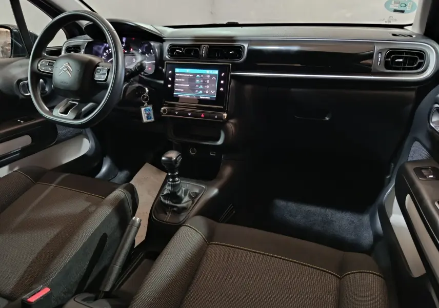 Vue intérieure avant de la Citroën C3 2024, tableau de bord noir avec écran tactile central et volant multifonctions.