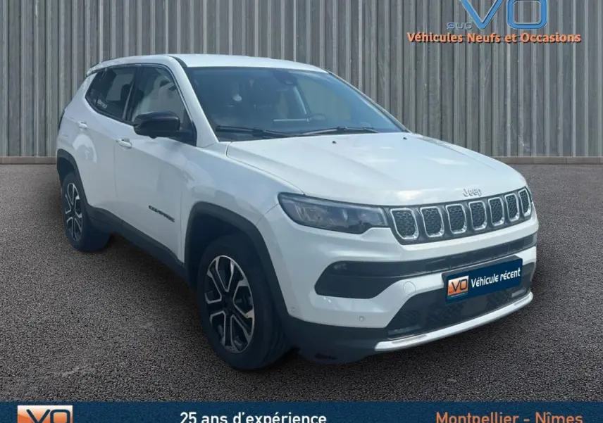 Jeep Compass blanc en 3/4 avant droit, avec jantes 17 pouces et calandre distinctive, stationné devant un mur métallique.
