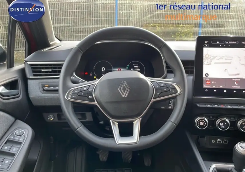 Vue intérieure centrée sur le volant de la Renault Clio rouge Désir Métal, avec tableau de bord numérique et écran tactile.