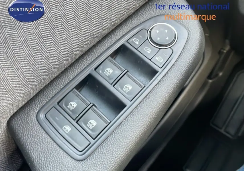 Gros plan sur les commandes des vitres électriques côté conducteur d’une Renault Clio 2025, tissu gris et plastique noir.