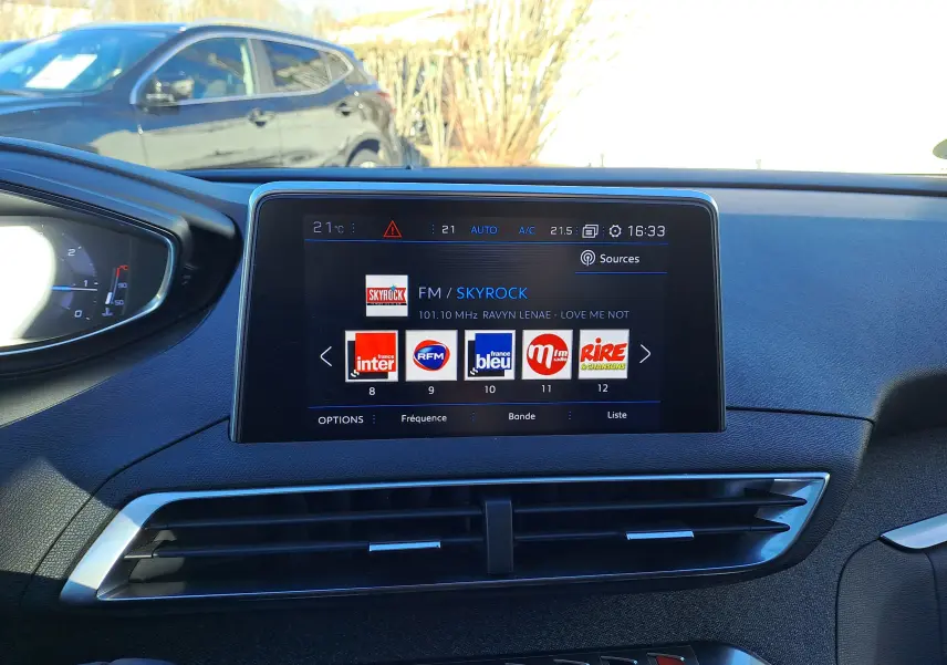 Vue intérieure centrée sur l'écran tactile du tableau de bord du Peugeot 5008 gris, affichant les stations radio FM.