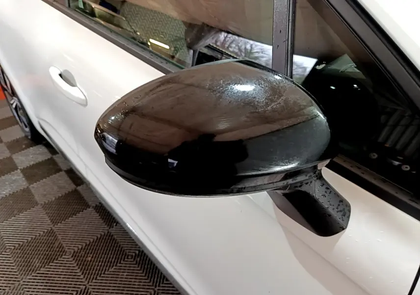 Rétroviseur noir en gros plan sur côté gauche d’une Renault Clio blanche vue de profil.