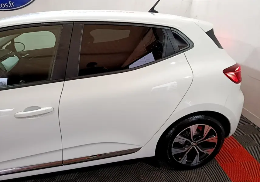 Vue latérale droite d'une Renault Clio blanche 2023 avec jantes alliage et vitres teintées, stationnée en intérieur.