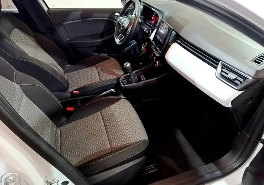 Vue intérieure côté conducteur de la Renault Clio Business blanche, montrant sièges, volant cuir et tableau de bord moderne.